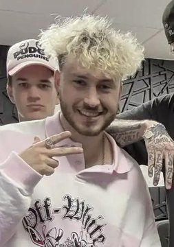 The image shows a young man with bleached curly blonde hair and a beard, smiling and flashing a peace sign while wearing a pink "Off-White" sweatshirt, with another person wearing a white "Dude Perfect" cap visible behind him. The image appears to be an older photo of the social media personality "ThreadGuy," whose recent bullish $10,000 price target on Zcash cryptocurrency is being highlighted in the post.