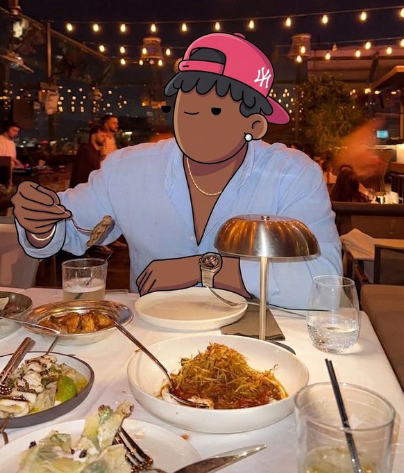 A person wearing a light blue shirt sits at a restaurant table with various dishes; their face is covered by a cartoon sticker of a person wearing a pink cap.