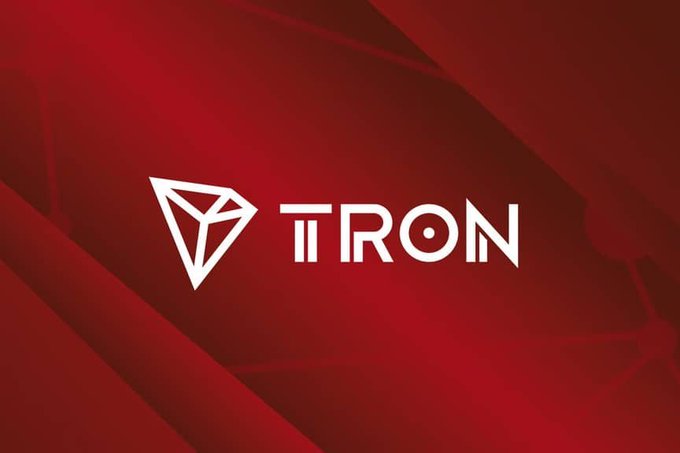 The image features the white TRON logo—comprising a geometric triangular emblem and the wordmark "TRON"—centered on a deep red background with subtle angular patterns. As a header for the post titled "Why TRON Continues To Lead Real-World Blockchain Adoption," the logo visually anchors the message, reinforcing the brand identity that the post credits with driving practical, real-world blockchain use.