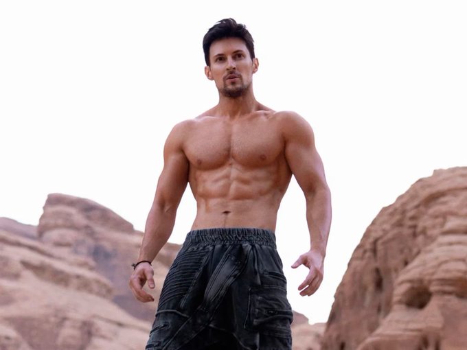 A shirtless, muscular man stands in a rugged desert landscape with rock formations in the background, his toned physique and confident pose conveying strength and power.

The image visually reinforces the bullish sentiment of the post, with the man's formidable, peak-condition physique serving as a metaphor for "strong" or "ripped" market gains, suggesting conviction in a long position.