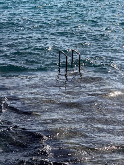 Metal pool ladder rails protrude from choppy, dark blue water.