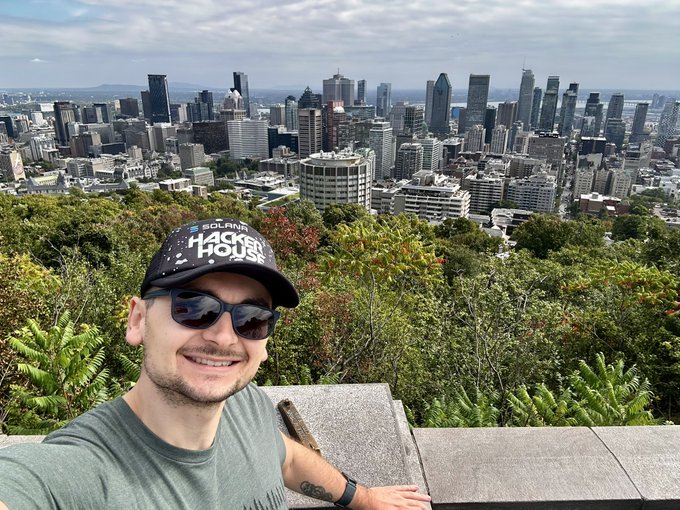 Selfie of a man wearing a 'Hard Hat' branded cap and sunglasses overlooking the Montreal city skyline from Mount Royal viewpoint.
