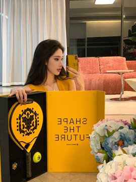 Photo of a woman with long dark hair holding a yellow 'Shape The Future' BNB branded shopping bag next to a bouquet of flowers.