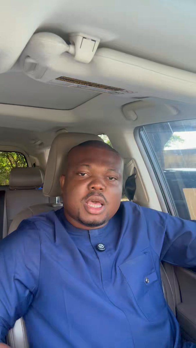 The image shows a man wearing blue clothing, sitting inside a car with his arms crossed over his chest. The car has its sunroof open, allowing natural light into the vehicle. There are no other people or objects visible in the photo. The caption reads "USDT is better in my Paystrater wallet. I do not trust banks", which seems to be unrelated to the main subject of the image and might even be a distraction from it.