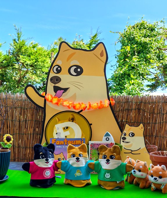 A collection of Fantom (Fantom) Shiba Inu merchandise, including plush toys and a large cardboard cutout, arranged in front of a bamboo fence and green trees.