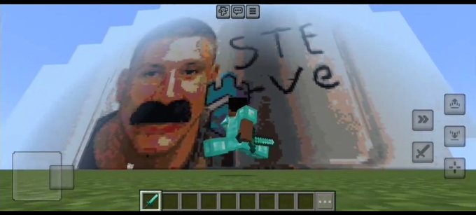 Minecraft gameplay screenshot showing a pixelated Steve face mural with 'STE +ve' written on a white pyramid structure, with in-game UI elements visible.