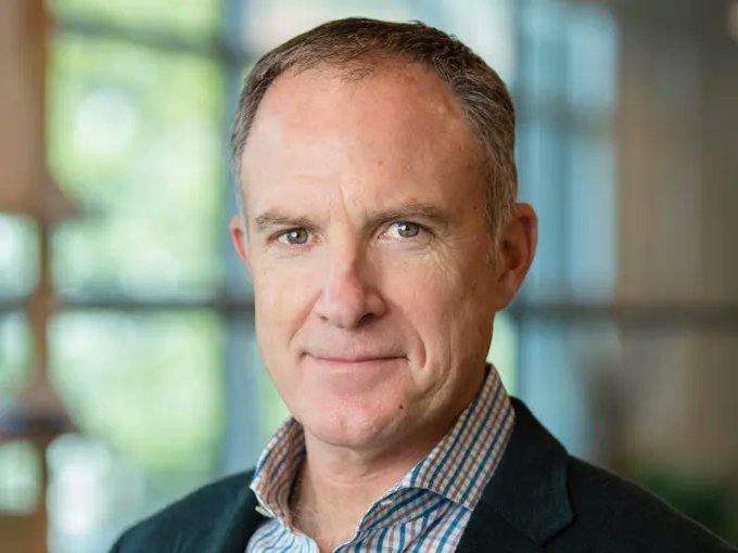 The image features a man wearing a suit jacket, standing against a blurred background that appears to be an office or workspace. The man has short hair and a beard, giving him a distinguished appearance. He is looking directly at the camera with a smile on his face. In the corner of the photo, there's text that reads "Ripple executive Jack McDonald says: $XRP adoption is ahead of schedule." This suggests that the man might be involved in the Ripple cryptocurrency project or has some knowledge about it.