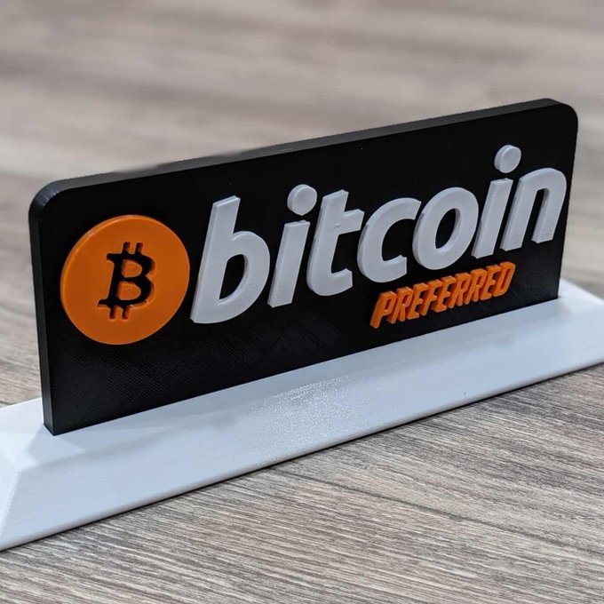 A 3D-printed sign displaying the Bitcoin logo and the text 'bitcoin PREFERRED' in white and orange lettering on a black background.