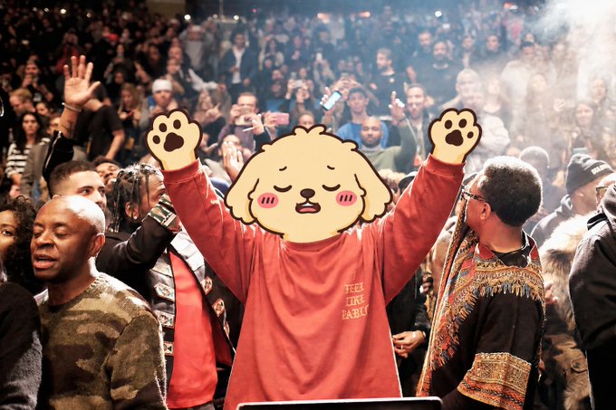 A person in a red sweatshirt with raised paw-like hands stands in a crowd, with their face obscured by a cute cartoon animal sticker overlay.