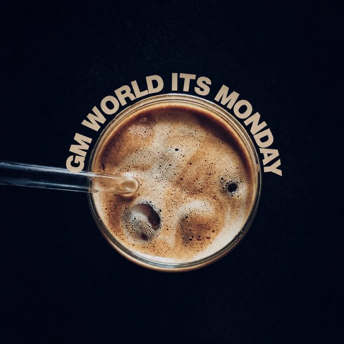 A top-down view of a frothy beverage in a glass with a glass straw, overlaid with the text "GM WORLD ITS MONDAY." The warm, cozy coffee imagery aligns perfectly with the casual "Gm fam" (good morning family) greeting.