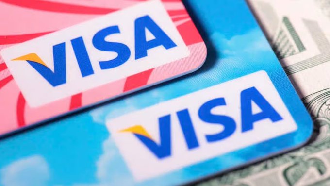 Two VISA credit cards, one pink and one blue, lie on top of US dollar bills.
