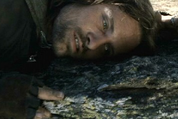 A close-up of actor Viggo Mortensen as Aragorn lying on the ground with a serious expression.