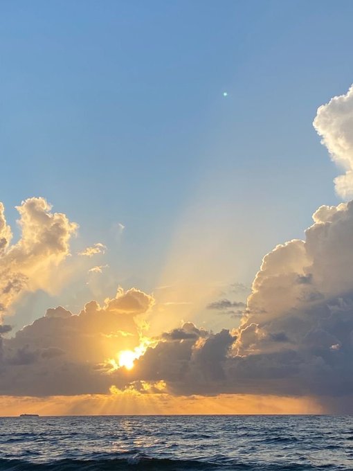 A serene seascape at sunset with golden sunlight breaking through dramatic clouds, casting rays over the rippling ocean water.