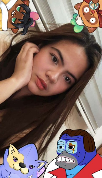 A young woman takes a selfie with several cartoon character filters, including a dog, cat, and blue cartoon face, overlaid on the image.