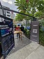 A person walks past a black promotional display banner set up on a city sidewalk near some outdoor tables.