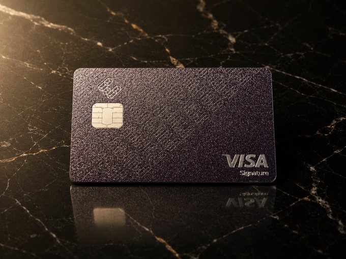 A dark purple textured Visa Signature credit card with an EMV chip rests on a glossy black marble surface, reflecting its image beneath.