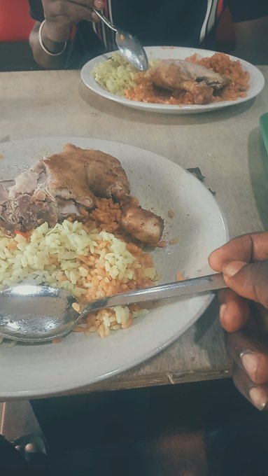 Two plates of food on a wooden table, featuring rice, beans, and what appears to be meat, with two people about to eat using spoons.
