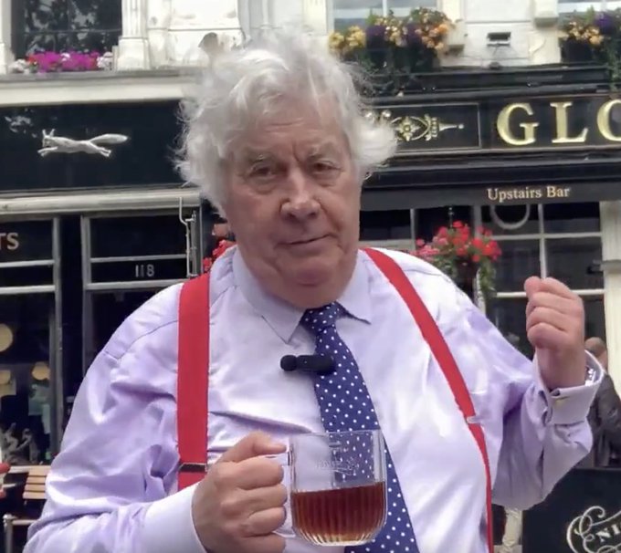 A distinguished older gentleman with wild white hair, wearing a lilac shirt, blue polka-dot tie, and bright red suspenders, holds a pint glass of beer outside what appears to be a pub with "GLOBE" and "Upstairs Bar" signage visible behind him. The image aligns with the post's reference to Breakpoint in London, capturing the celebratory spirit of the 69-year-old's age milestone while presumably toasting to the crypto community gathering.