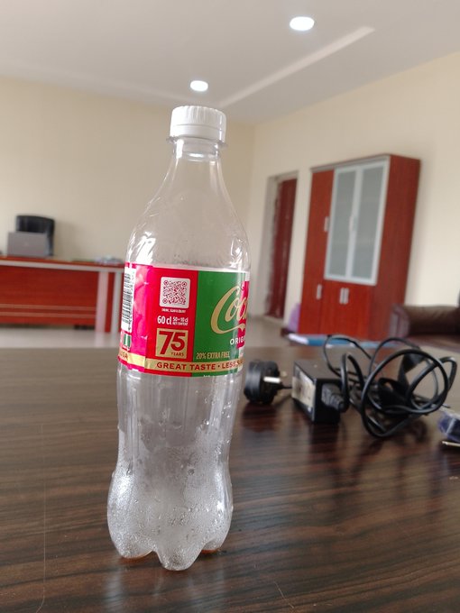 An empty 60cl Coca-Cola bottle on a wooden table in what appears to be an office or home setting.