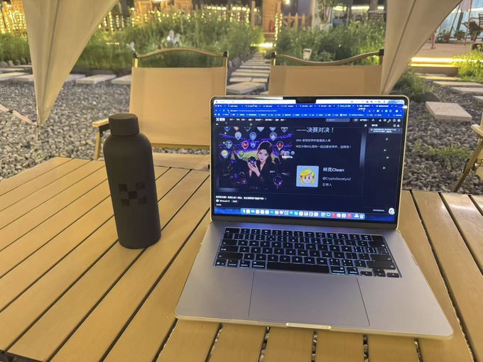 A silver laptop open on a wooden outdoor table displaying what appears to be a Chinese streaming page, next to a black water bottle.