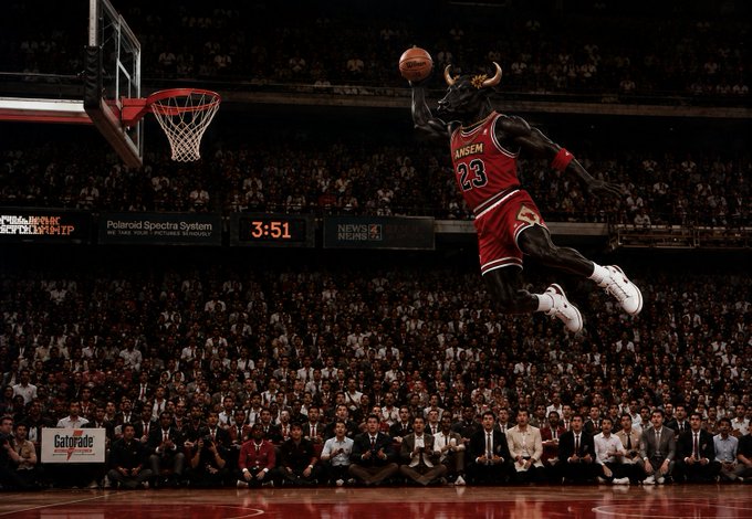 A basketball player wearing a red 'Jansen 23' Bulls jersey is captured mid-air performing a slam dunk in front of a packed arena crowd.