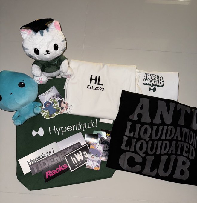 A collection of Hyperliquid merchandise is displayed, including a plush cat wearing a graduation cap, a green tote bag with the "Hyperliquid" logo, a white "HL Est. 2023" shirt, and a black "Anti Liquidation Liquidated Club" shirt, alongside various stickers and cards. The image ties to the post as a showcase of branded swag likely gathered or earned through community events and volunteering efforts.