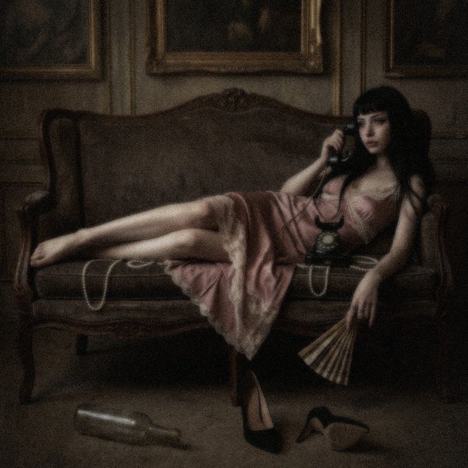 A painting of a young woman in a pink slip dress reclining on a vintage sofa while holding a rotary telephone receiver, with a fallen bottle and shoes nearby.
