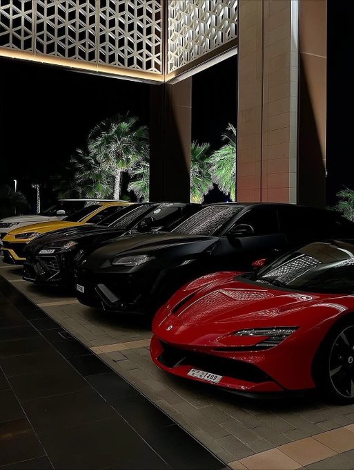 The image features five luxury sports cars parked next to each other, including four red sports cars and one black car. The cars are positioned at an angle, with some facing towards the front of the scene while others face towards the back. The cars appear to be in excellent condition, suggesting that they might belong to a high-end automobile brand or dealership.