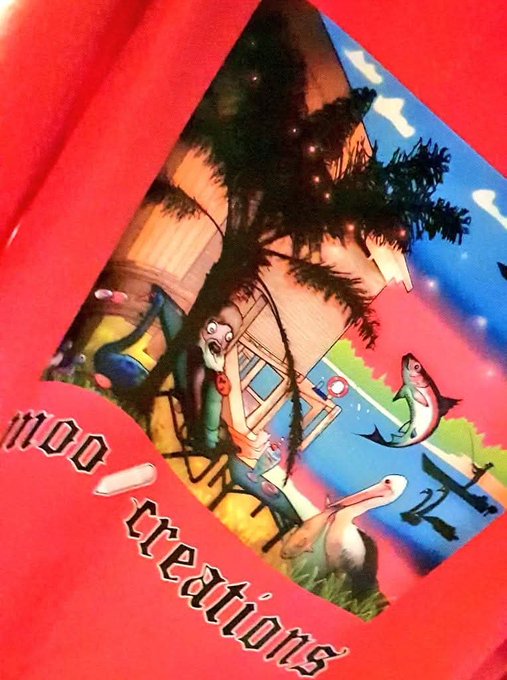 A photograph of a red t-shirt featuring a colorful graphic design with characters, a house, palm trees, fish, and birds, along with the gothic-style text 'moo creations'.