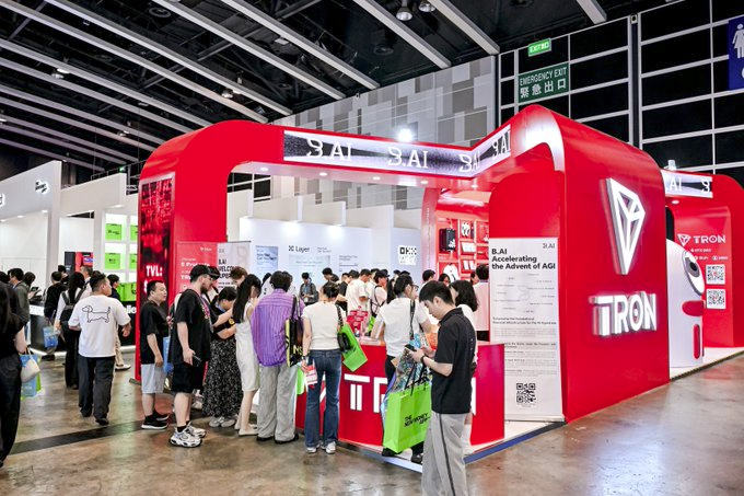 In this scene, there is an expo floor where several people are gathered around a booth representing Tron, a company known for its technology products. The booth features a red sign with white text that reads "START S." This indicates that the event is centered on the theme of starting something new or embarking upon a journey in the technology industry. Multiple individuals can be seen at this booth, possibly engaging in conversations, exploring Tron's offerings, and collecting information about the company. The overall atmosphere seems to be bustling with activity as people interact with the booth and enjoy being part of the event experience.