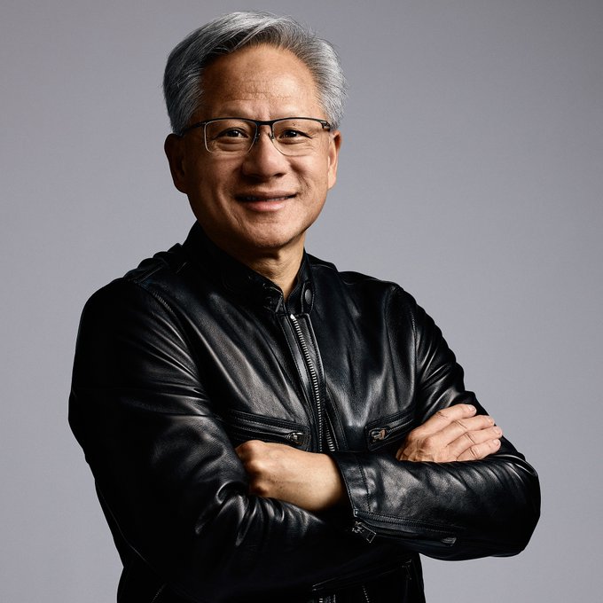Nvidia CEO Jensen Huang, dressed in his signature black leather jacket and glasses, smiles confidently with arms crossed. The image accompanies his comments dismissing AI doomsday fears as "completely false" and designed merely to grab attention.