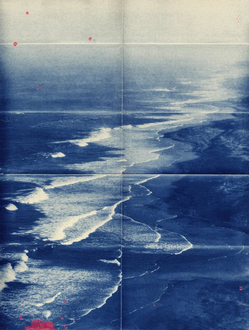 An aerial, blue-tinted view of ocean waves breaking along a shoreline, presented with a vintage, creased paper texture.