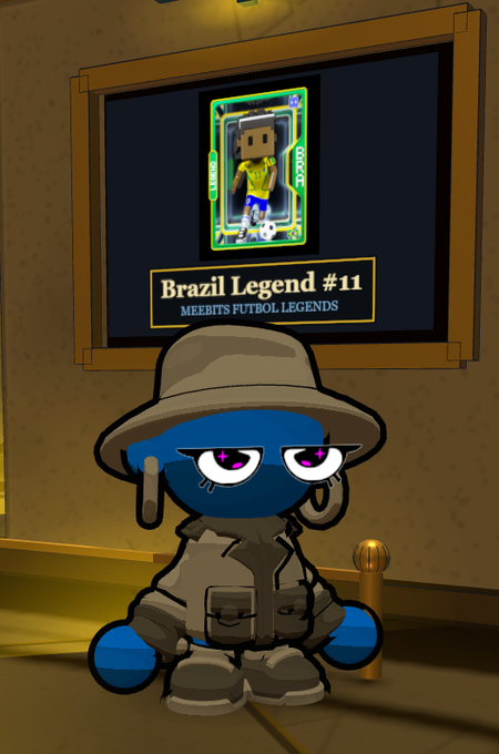 A cartoon blue character wearing a safari hat and trench coat stands in front of a framed picture displaying 'Brazil Legend #11 MEEBITS FUTBOL LEGENDS' featuring a soccer player card.