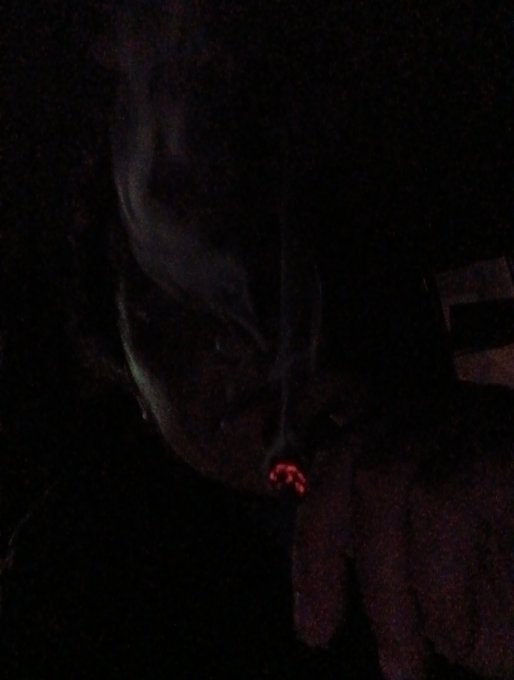 A very dark, low-quality photograph appears to show a person's face with a small red glowing light visible.