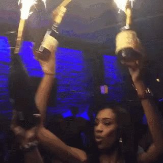 The image shows a woman with long hair standing up, holding two champagne bottles above her head as if she's about to celebrate or toast something. There are other people present in the scene, but they are not the main focus of the photo. The caption "Just use Jupiter" suggests that this might be related to a social media post or event where the woman is celebrating with friends or family using a popular brand like Jupiter.