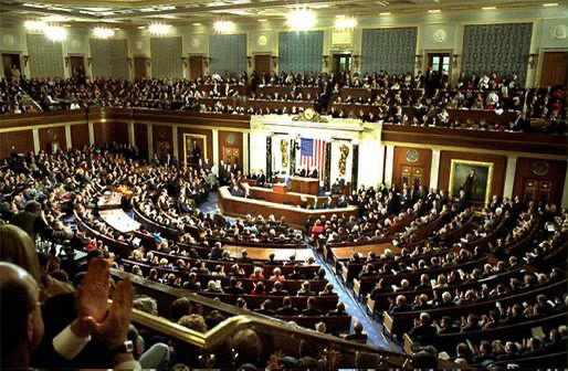 The interior of a crowded legislative chamber or congress hall with a speaker at the podium, surrounded by hundreds of attendees in tiered seating.