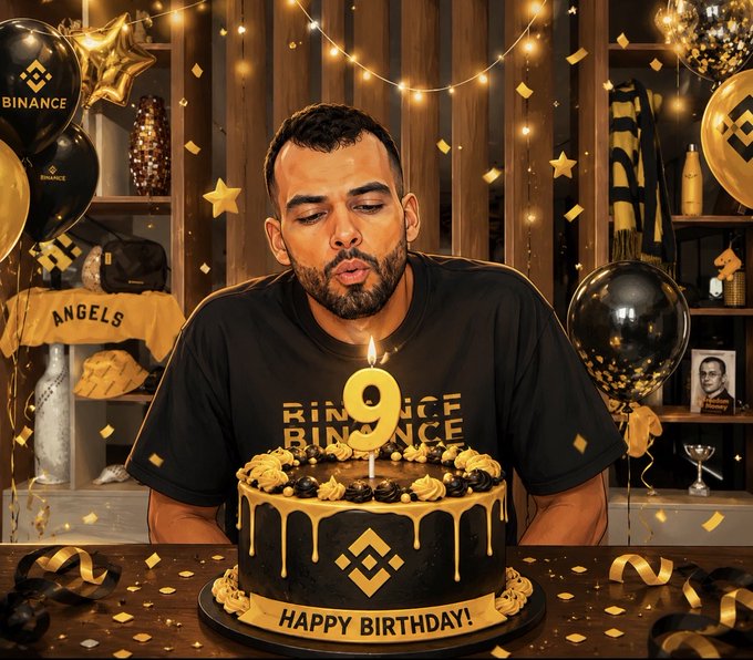 A man wearing a black 'BINANCE' t-shirt is blowing out a candle shaped like the number '9' on a black and gold birthday cake that reads 'HAPPY BIRTHDAY!', surrounded by black and gold 'BINANCE' balloons and confetti.