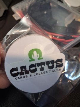 A hand holding a circular white sticker with a green cactus logo that reads 'CACTUS CARDS & COLLECTIBLES' over a plastic bag.