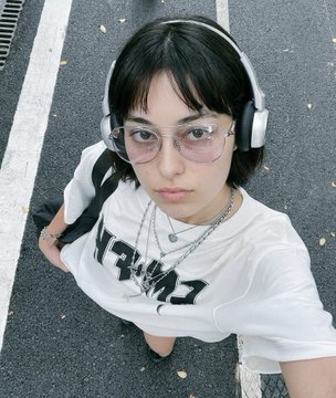 A young woman with short dark hair, large glasses, and headphones wearing a white t-shirt, photographed from above.
