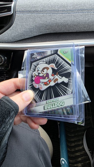 A hand holding a card protector sleeve containing a trading card featuring an angry cartoon dog labeled 'BAD ASS BULLDOG'.