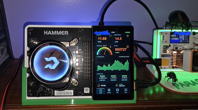 A Bitcoin mining setup featuring a HAMMER brand miner with a glowing blue fan next to a smartphone displaying mining statistics including 11.68 TH/S and 14.5 J/TH.