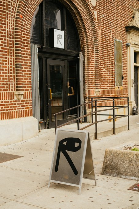 The image features an outdoor scene with a brick building that has a sign for "R" on its front door. The sign also displays the words "Public Records". A woman can be seen walking past the entrance of this venue, which appears to be hosting a special event or concert at night.