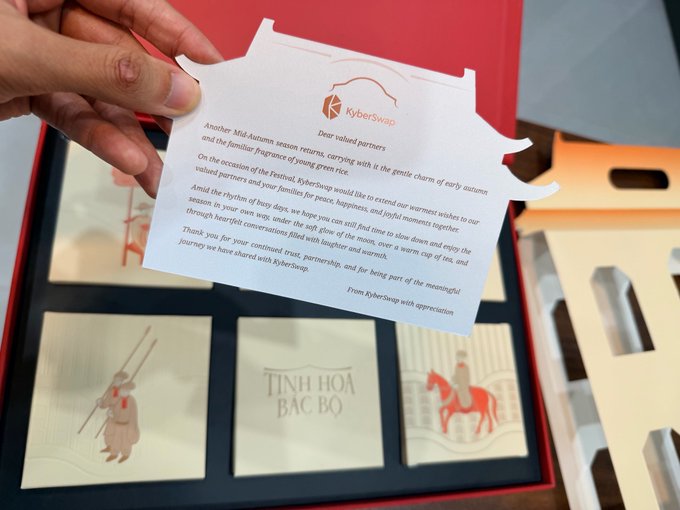 A hand holding a KyberSwap thank-you card with text thanking partners for Mid-Autumn season, above an open gift box containing items labeled "TINH HOA BẮC BỘ" with illustrations of people on horseback.