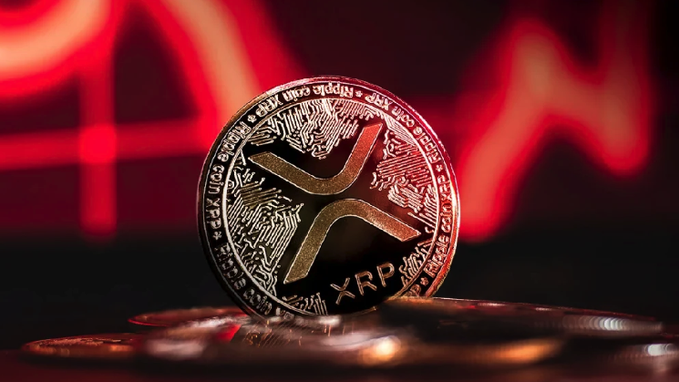 A physical representation of an XRP cryptocurrency coin stands upright against a dramatic red-lit background featuring a downward-trending line graph, symbolizing XRP's recent price drop below $1. The metallic coin prominently displays the XRP logo and surrounding text, visually reinforcing the article's theme of declining value amid Ripple's expanding institutional adoption.