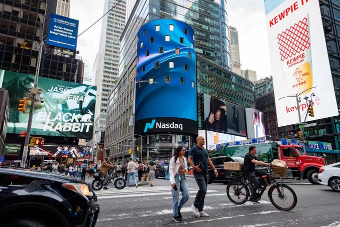 The image depicts Times Square in New York City, showcasing the iconic Nasdaq stock market building with its large blue digital screens and the "Nasdaq" logo prominently displayed. Surrounding billboards advertise various brands including "Black Rabbit," "Jason Bateman," "Kewpie" mayonnaise, and "Starbucks Coffee," while pedestrians and cyclists navigate the busy intersection below.

The accompanying post discusses tokenized stocks and Robinhood Chain going mainnet in July, noting that while some on Crypto Twitter (CT) claim tokenized stocks are a single product, there are actually two different versions attached to the same tickers that don't provide the same claims. The image connects to this discussion by visually representing the traditional stock market through the Nasdaq building, contrasting the centralized, physical-world financial infrastructure with the newer decentralized tokenized stock products being discussed.