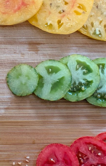 Three rows of thinly sliced tomatoes—a yellow variety at the top, green in the middle, and red at the bottom—are arranged on a wooden cutting board, with the green tomato in the center humorously resembling a radioactive "nuke" to match the caption's playful reference.