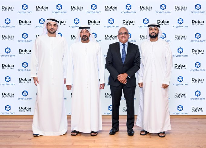 Four men pose for a photo at a Dubai Duty Free and crypto.com branded backdrop, with three wearing traditional Emirati attire and one in a black suit, marking the launch of Crypto.com Pay as a new regulated digital payment option at Dubai Duty Free.