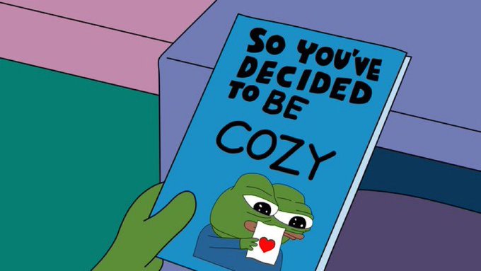 A green hand holds up a blue book titled "So you've decided to be COZY" featuring a sad Pepe the Frog holding a love letter. The image humorously suggests that someone greeting others with "Gm frens" (good morning friends) has committed to embracing a cozy, wholesome lifestyle—Pepe appearing tearful yet affectionate, clutching a heart-decorated card.