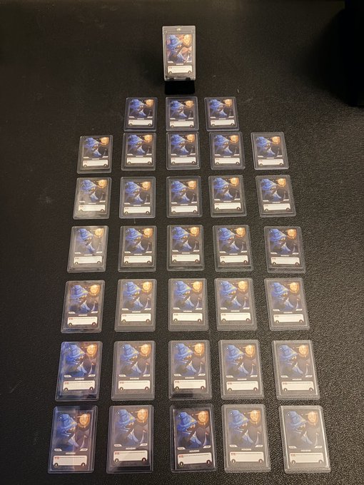 Multiple trading cards in protective sleeves arranged in a pyramid pattern on a dark surface, each card displaying the same character image.