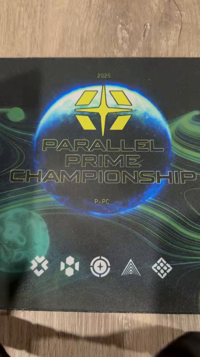 The image features a black and green poster with white text that reads "Parallel Prime Championship". The poster has a unique design, featuring a blue planet surrounded by yellow stars. There are also symbols of various shapes and colors scattered throughout the poster. In addition to the main elements on the poster, there is a small logo in the bottom left corner.